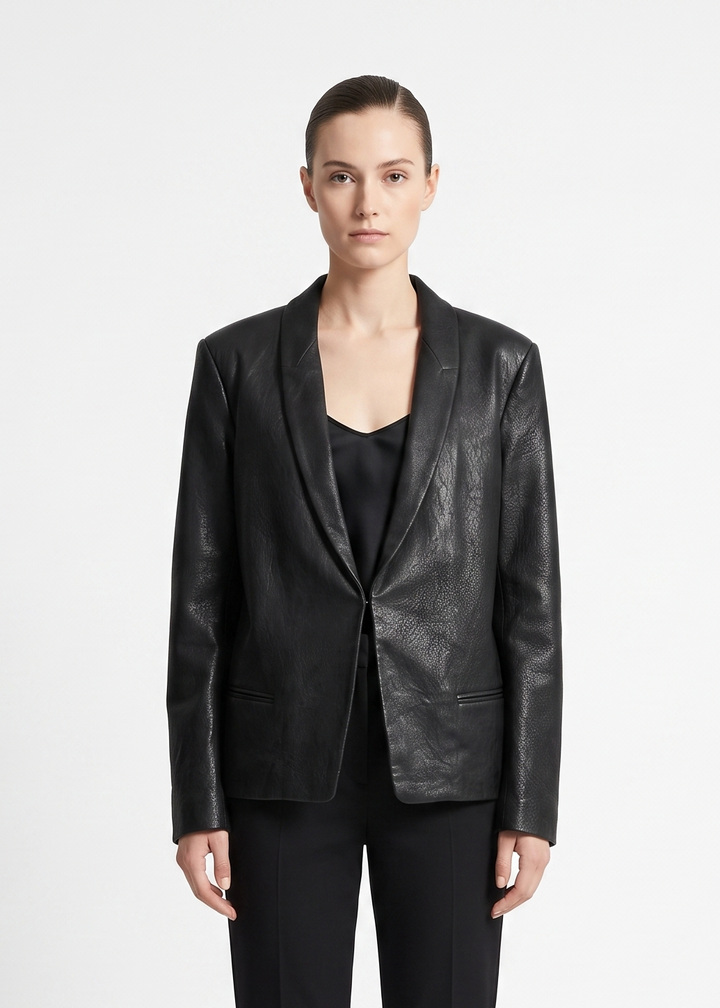 A model wearing a black textured leather blazer with shawl lapels over a black top and black trousers, photographed against a plain light gray studio background.