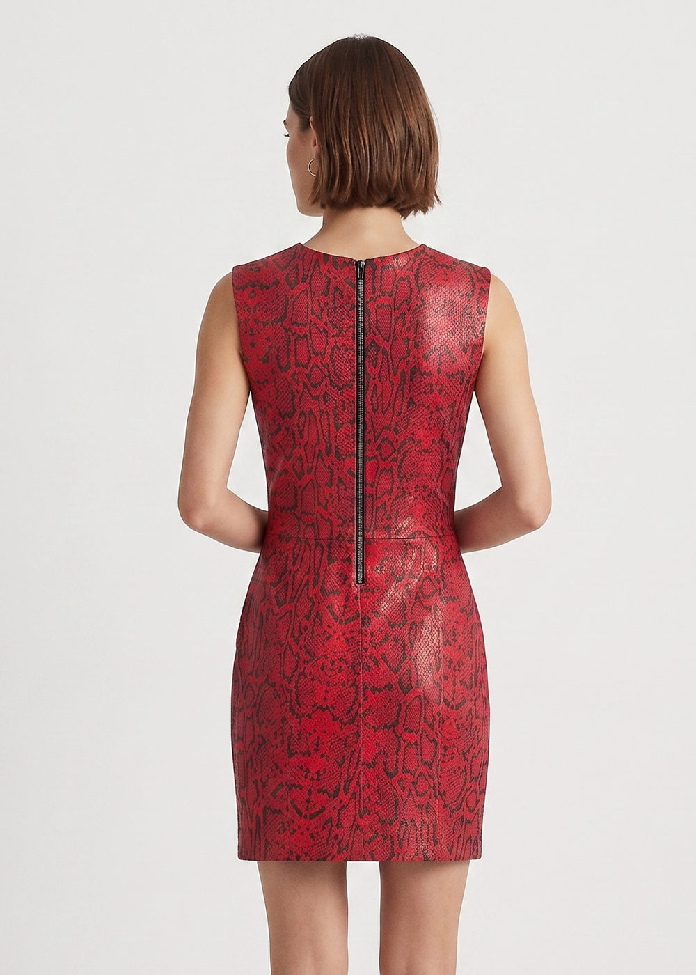 A woman viewed from the back wearing a sleeveless red dress with a black snakeskin-style pattern and a black center zipper, paired with black heels, against a plain light gray studio background.