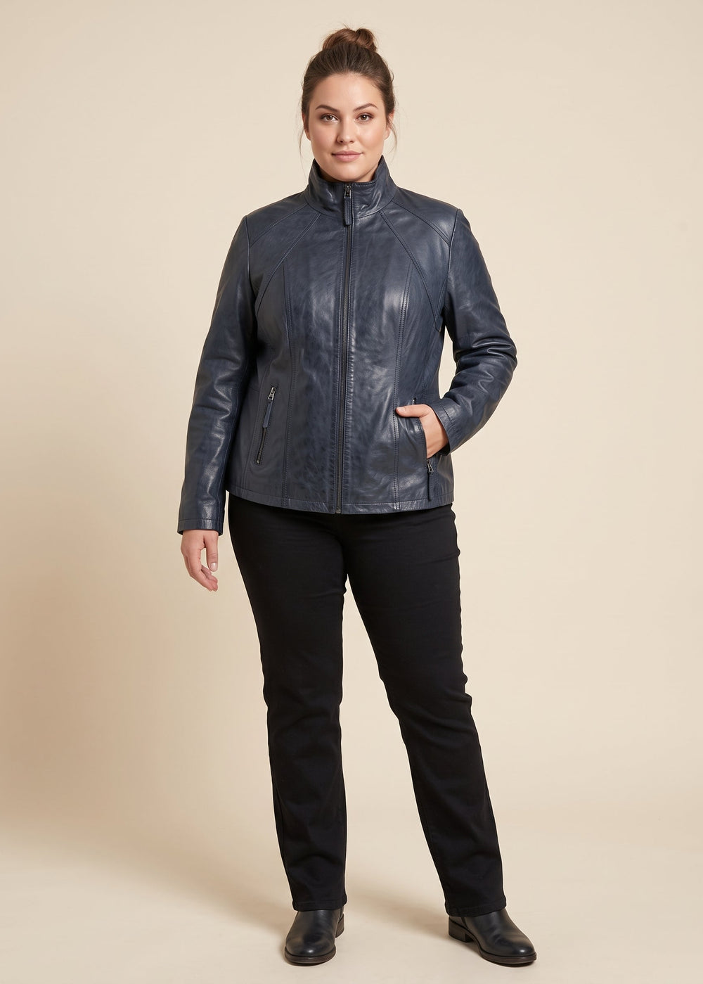 A woman modeling a dark navy blue genuine-leather jacket with a high collar and front zipper, paired with black pants, against a solid beige studio background.