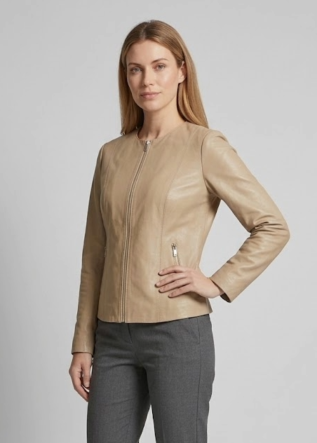 A woman modeling a beige -leather jacket and dark gray trousers against a light gray studio background.